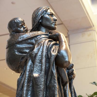 bronze statue of a woman holding her baby on her back in a swaddled cloth